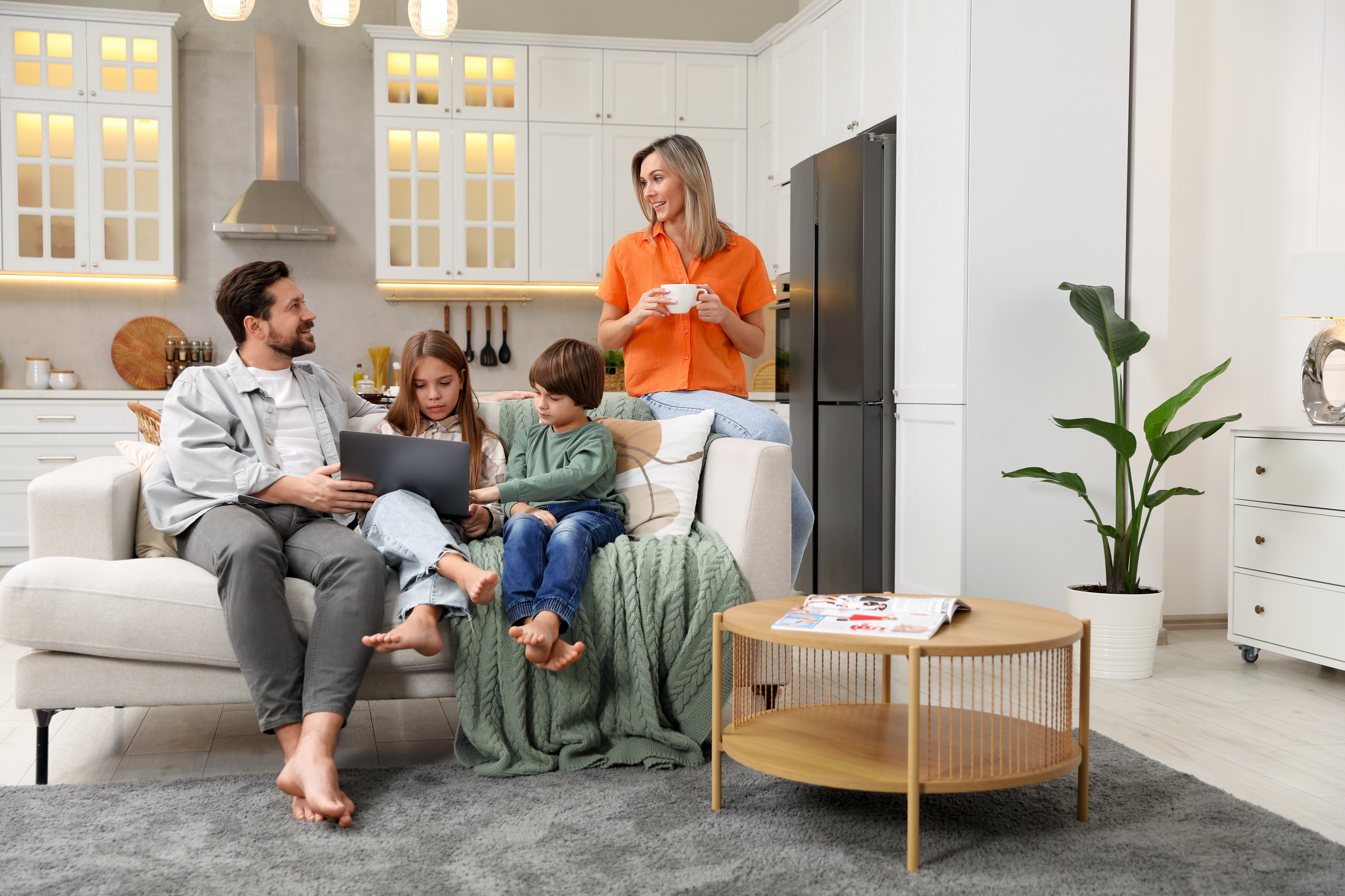 Happy family with laptop spending time together on sofa in kitchen at home